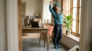 Person stretching beside a sunlit window during a break from desk work